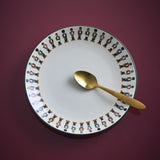 Jolly Stoneware Christmas Side Plate in cream with a ring of nutcracker soldiers around the rim, shown with a gold spoon on a dark red background.