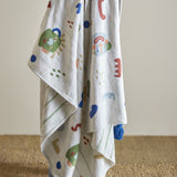 Sylvie Cotton Throw in Multi draped over a chair, showing a cotton-blend blanket printed with abstract shapes, dots and curves in red, green, blue and ochre, with a blue tassel corner detail.