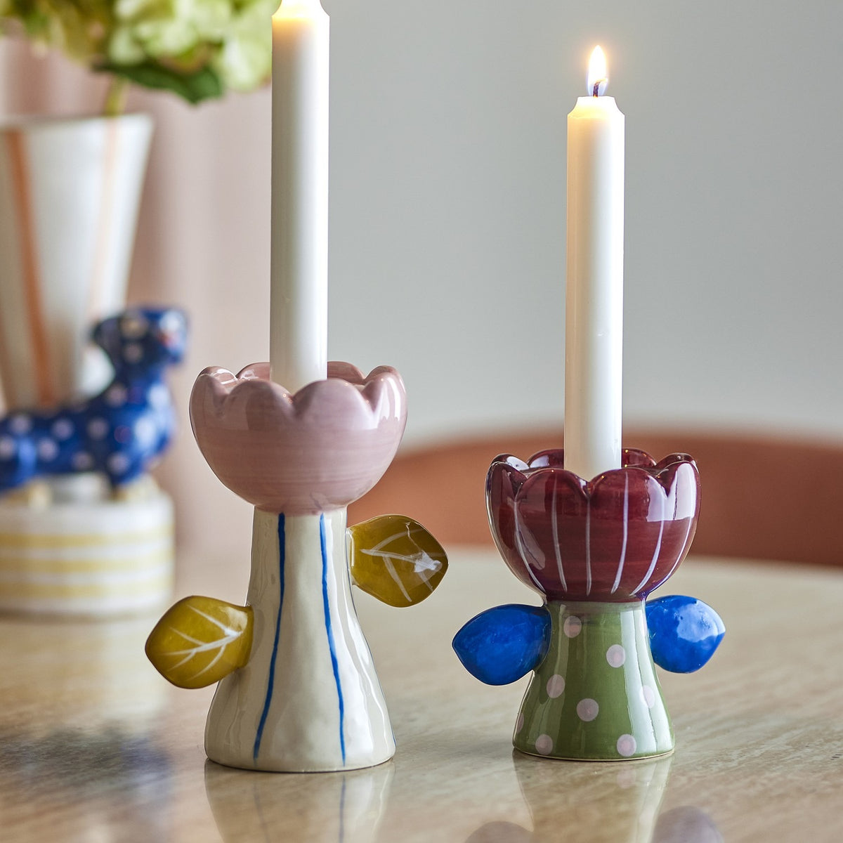 Florita Flower Candle Holders set of 2 in handpainted ceramic, pink and burgundy scalloped flower cups with leaf details on striped and polka-dot stems, holding white taper candles on a table.