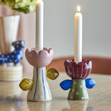 Florita Flower Candle Holders set of 2 in handpainted ceramic, pink and burgundy scalloped flower cups with leaf details on striped and polka-dot stems, holding white taper candles on a table.