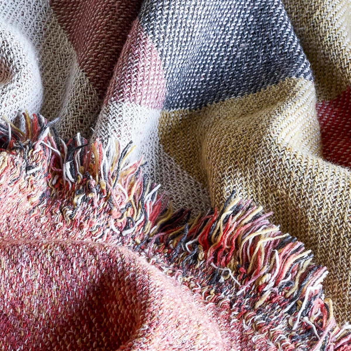 Close-up of the Arni Throw in Multi, a woven fabric throw with a check pattern in pink, mustard, navy and cream, finished with a thick mixed-yarn fringe.