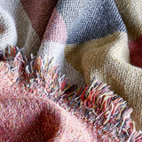 Close-up of the Arni Throw in Multi, a woven fabric throw with a check pattern in pink, mustard, navy and cream, finished with a thick mixed-yarn fringe.