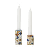 Set of two cylindrical stoneware candle holders in tall and short sizes, each decorated with a multicoloured bird and floral pattern, holding white taper candles on a plain white background.