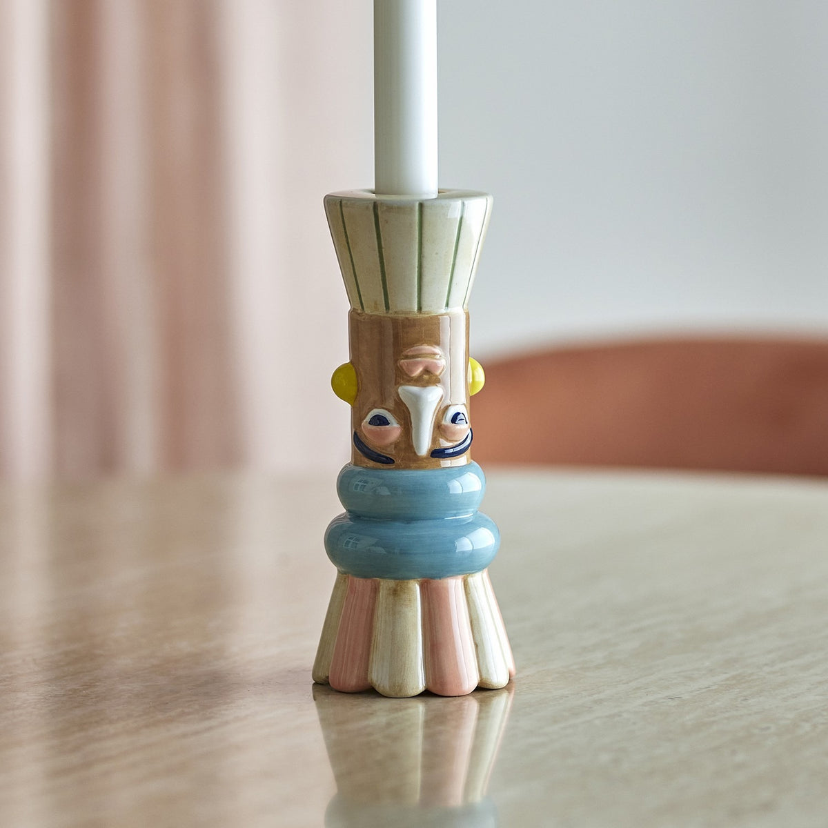 Minio Ceramic Vase 17cm in Multi used as a candle holder with a white taper candle, featuring a hand-painted face, blue banded neck, and fluted pink and cream base on a tabletop.