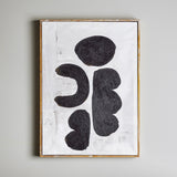 Comma Wooden Framed Print in Black, featuring four rounded abstract black forms with a textured, grainy surface on a brushed white canvas, set in a slim firwood frame against a plain grey wall.