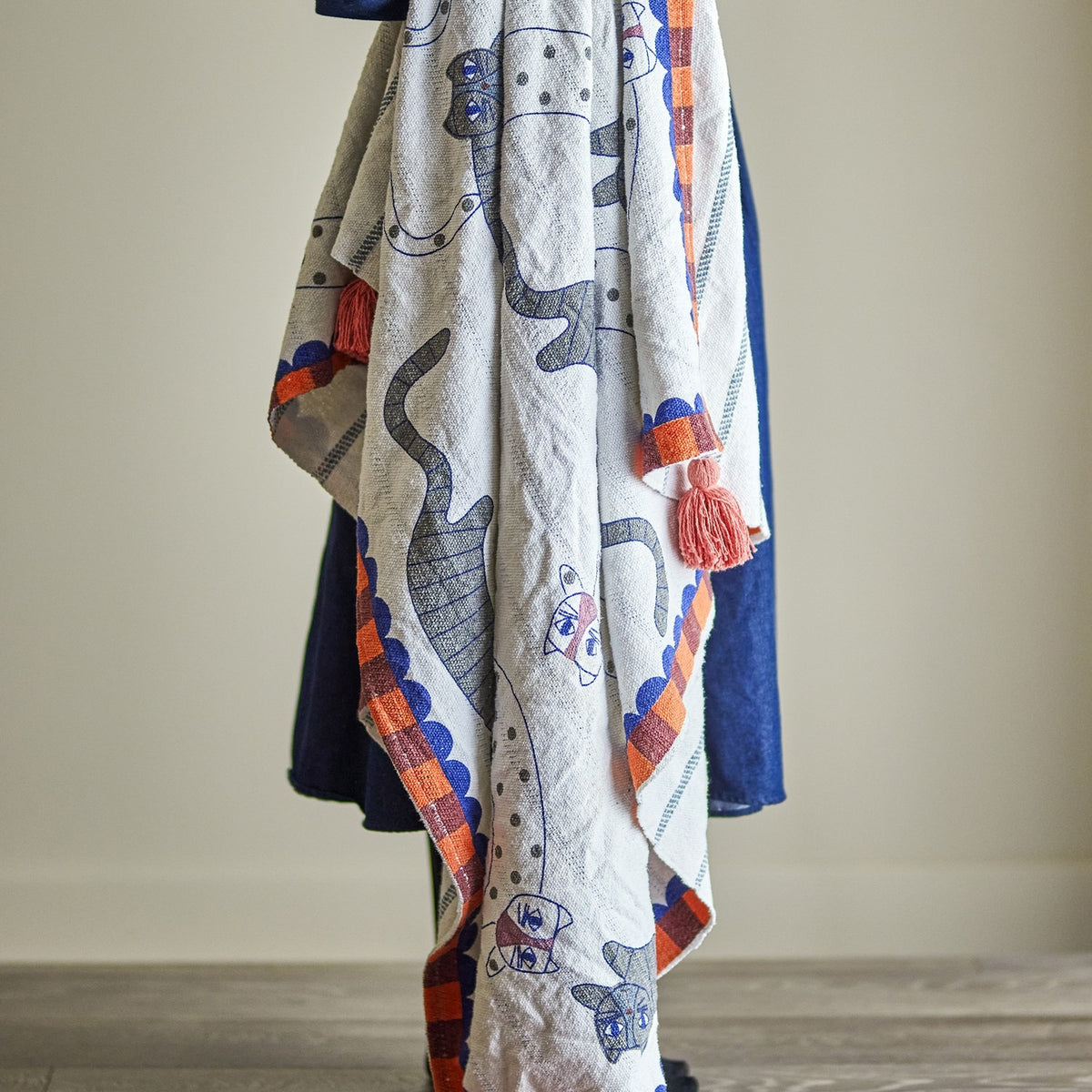Missy Striped Throw in Multi draped over a chair, cotton blend fabric with outlined cat motifs, scalloped edge, checked border, and corner tassels.