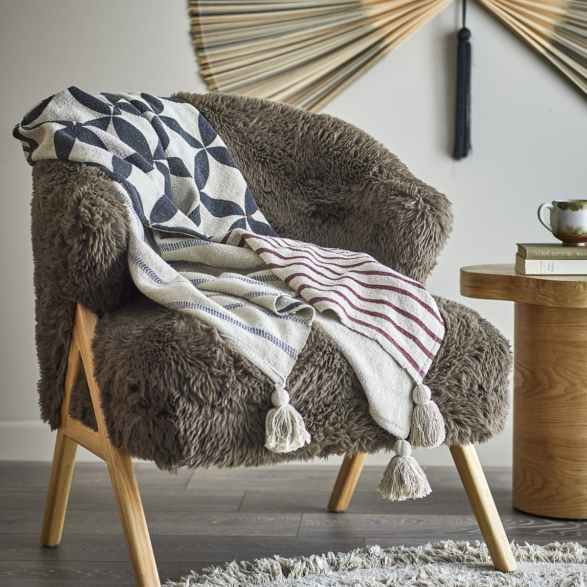 Forma Striped Throw in beige with interlocking oval lattice print and striped reverse, draped over a fluffy brown armchair with wooden legs.