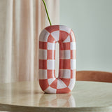 Mae Ceramic Vase 32cm in Orange, a tall ceramic loop shape with a handpainted orange and white check pattern, holding a single green stem on a wooden table.