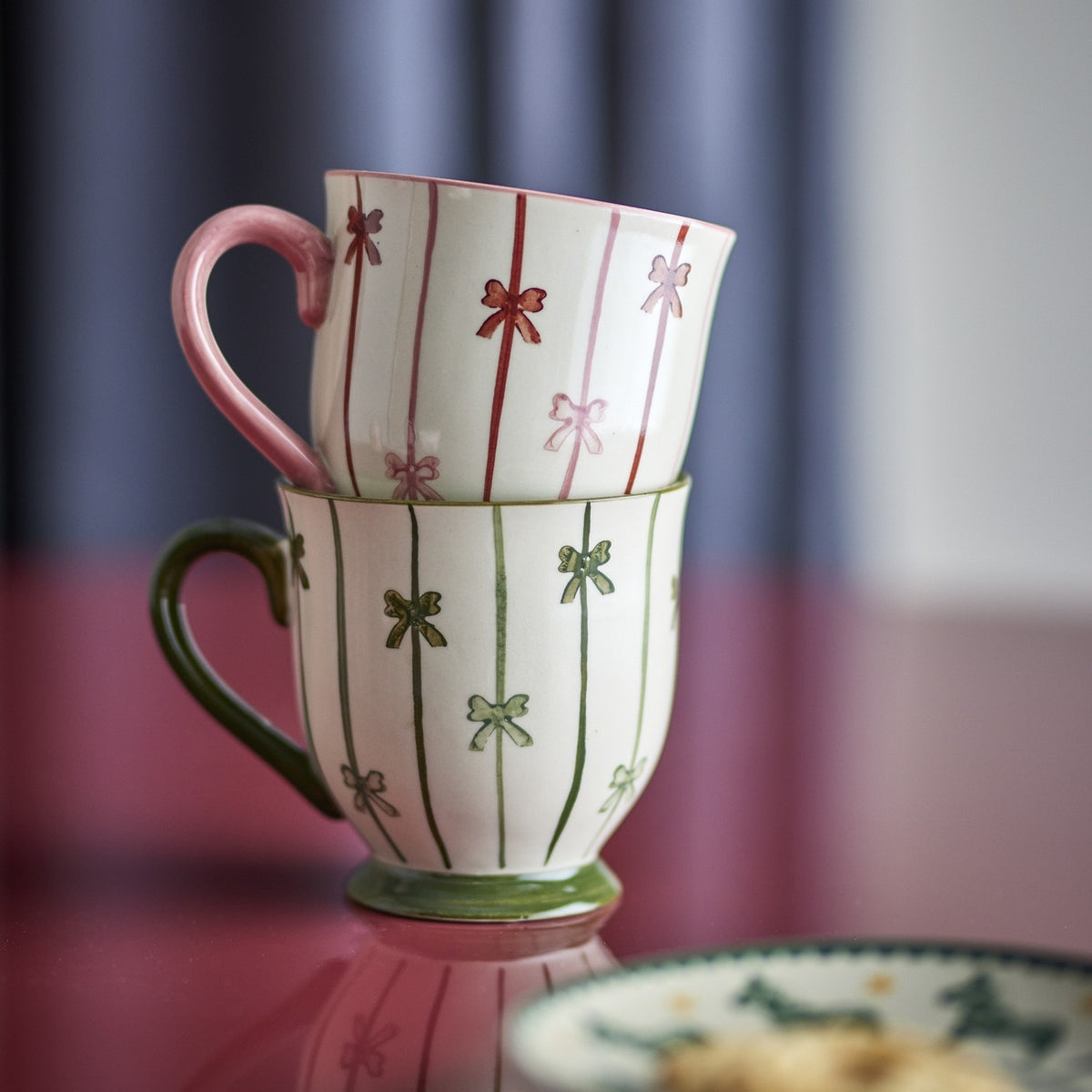 Hope Striped Stoneware Christmas Mugs, set of 2, stacked ceramic mugs with pink and green vertical stripes, hand-painted bows, curved handles and footed bases.