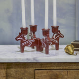 Siffer Resin Advent Candle Holder in red, four joined horse figures with hand-painted folk detailing, each holding a white taper candle, shown on a marble surface.