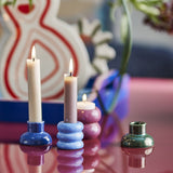Tana Speckled Tealight & Candle Holders in stacked ribbed blue and pink ceramic, shown lit with a green candle holder nearby on a reflective tabletop.