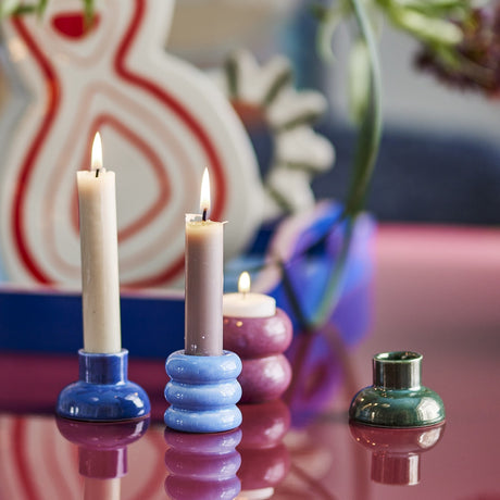 Tana Speckled Tealight & Candle Holders in stacked ribbed blue and pink ceramic, shown lit with a green candle holder nearby on a reflective tabletop.