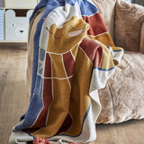 Sun Cotton Throw in multicoloured woven cotton blend, draped over a beige armchair, featuring a smiling sun design with rays, stars, and tasselled edge.