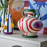 Betiva Striped Stoneware Vase 25.5cm in white and red with a purple spot motif and green rim handles, shown on a sideboard with a smaller striped vase and patterned wall art.