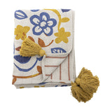 Figuria Cotton Throw folded flat with a multicoloured floral, leaf and bird print in blue, mustard and rust tones, finished with mustard corner tassels, shown on a white background.