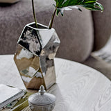 Dimona Stoneware Vase 23cm in silver, faceted mirrored finish holding a green leaf, styled on a wooden table beside a lidded trinket box.