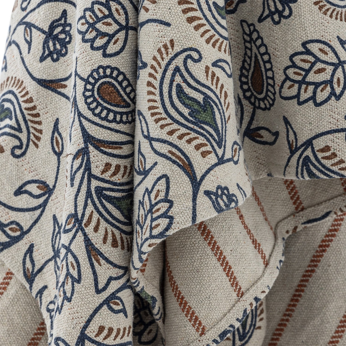 Close-up of the Paisley Floral Cotton Throw in multi, showing navy and rust paisley and floral print on draped fabric with a striped reverse side visible.