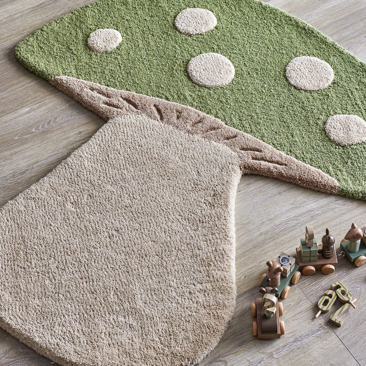 Mushroom Wool Rug 90x85cm in green with raised cream spots, gill detailing and a cream stem, shown on a wooden floor beside wooden toys.