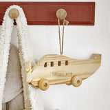 Plane Wooden Baby Mobile in natural pine, hanging by hemp cord from a peg rail, showing propeller nose, tail fin, window cut-outs, wings and wheels.