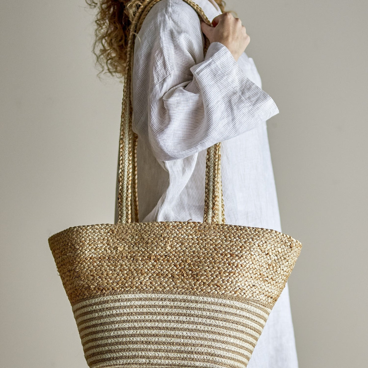 Simona Jute Shopping Bag in natural, worn on the shoulder, showing woven braided handles, a chunky textured upper body, and a striped lower band in jute.
