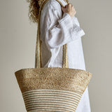 Simona Jute Shopping Bag in natural, worn on the shoulder, showing woven braided handles, a chunky textured upper body, and a striped lower band in jute.