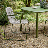 Calana Iron Garden Chair in grey, with woven basketweave cord seat and back, curved armrests and green metal frame, shown outdoors beside a green garden table on gravel.