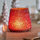 Filiz glass Christmas tealight holder in gold, tapered round shape with dense raised mosaic texture, lit candle glowing inside near blurred Christmas trees.