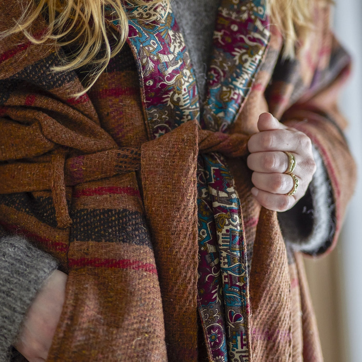 Rieti Kimono in brown, close-up of tie belt and striped woven fabric with patterned lapel lining visible, worn with hand resting at the waist.