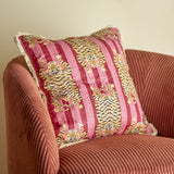 Poirino Cotton Cushion in pink with striped tiger print, fringed edges and visible running stitch detail, shown on a rust corduroy armchair.