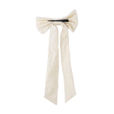 Ruby Cotton Christmas Bow in cream woven cotton with two full loops and long trailing tails, secured by a black clip, shown on a plain white background.