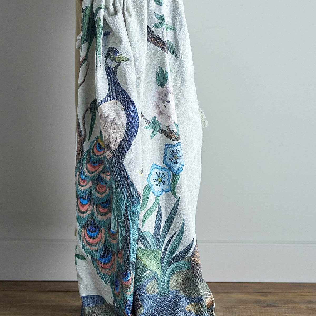 Peacock Throw in green polyester-cotton blend, draped to show a printed peacock, flowering branches and foliage design, against a plain light background.