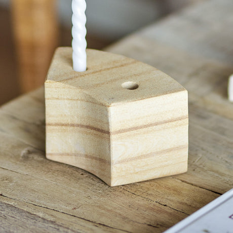 Florida Sandstone Candle Holder in beige, a chunky faceted block with two taper candle openings, holding a white twisted candle on a wooden surface.