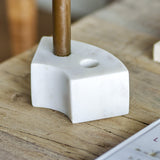Florida Marble Candle Holder in white, a curved low block with two candle holes, shown holding a brass candlestick on a wooden table.