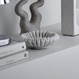 Harmonia Marble Bowl 17.5cm in white with ridged, scalloped petal-like rim, shown on a shelf beside a textured grey sculpture and stacked books.