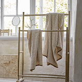 Malou Cotton Towel in Natural with raised diamond pattern, shown draped over a bamboo rail beside a window in a bright room.