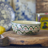 Karlie Stoneware Bowl 15cm in Green, a round ceramic bowl with hand-painted green arches, dotted bands and scalloped patterns, plain glazed interior, shown on a wooden board.