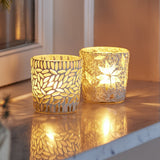 Myr glass tealight holders, set of 2 in white, one with a leaf mosaic design and one with a beaded star pattern, shown lit on a marble surface.