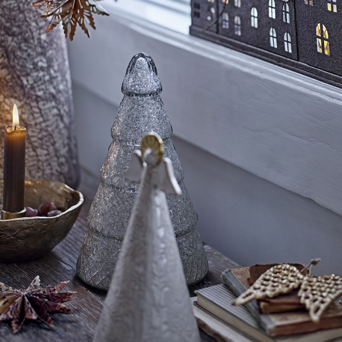 Emilius glass Christmas tree decoration in white, tiered fir shape with rounded tip, displayed on a wooden shelf among candles, books and festive ornaments.