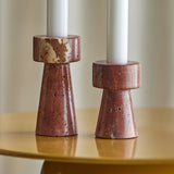 Anneli Travertine Candle Holders Set of 2 in Brown, two tapered stone bases with round collars holding white candles, shown at different heights on a glossy mustard table.