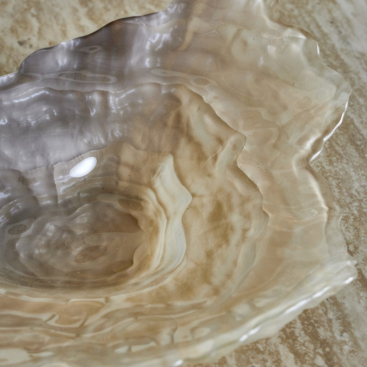 Aiku Shell Glass Bowl 38x29cm in Pearl, a wide shallow glass bowl with a ruffled rim, stepped ridges, and a textured centre, shown in close-up on a marble surface.