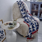 Rimme Cotton Throw in multicoloured navy and cream wave print with red border and fringed edge, draped over a cream shaggy armchair in a living room setting.