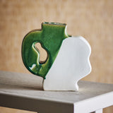 River Crackle Stoneware Vase 20cm in green and white, flat-sided with a wavy profile, narrow neck and open handle cut-out, shown on a table against a woven backdrop.