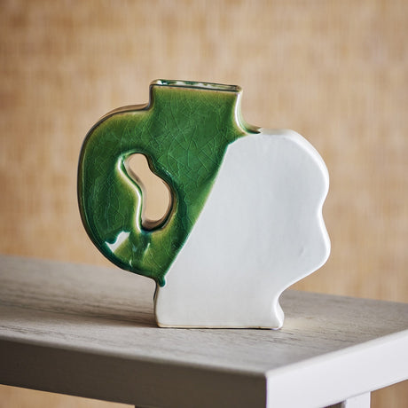 River Crackle Stoneware Vase 20cm in green and white, flat-sided with a wavy profile, narrow neck and open handle cut-out, shown on a table against a woven backdrop.