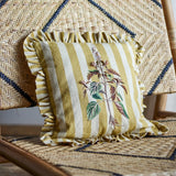 Camila Striped Cotton Cushion in yellow, square with ruffled edge, embroidered botanical stem design, shown on a woven rattan chair.