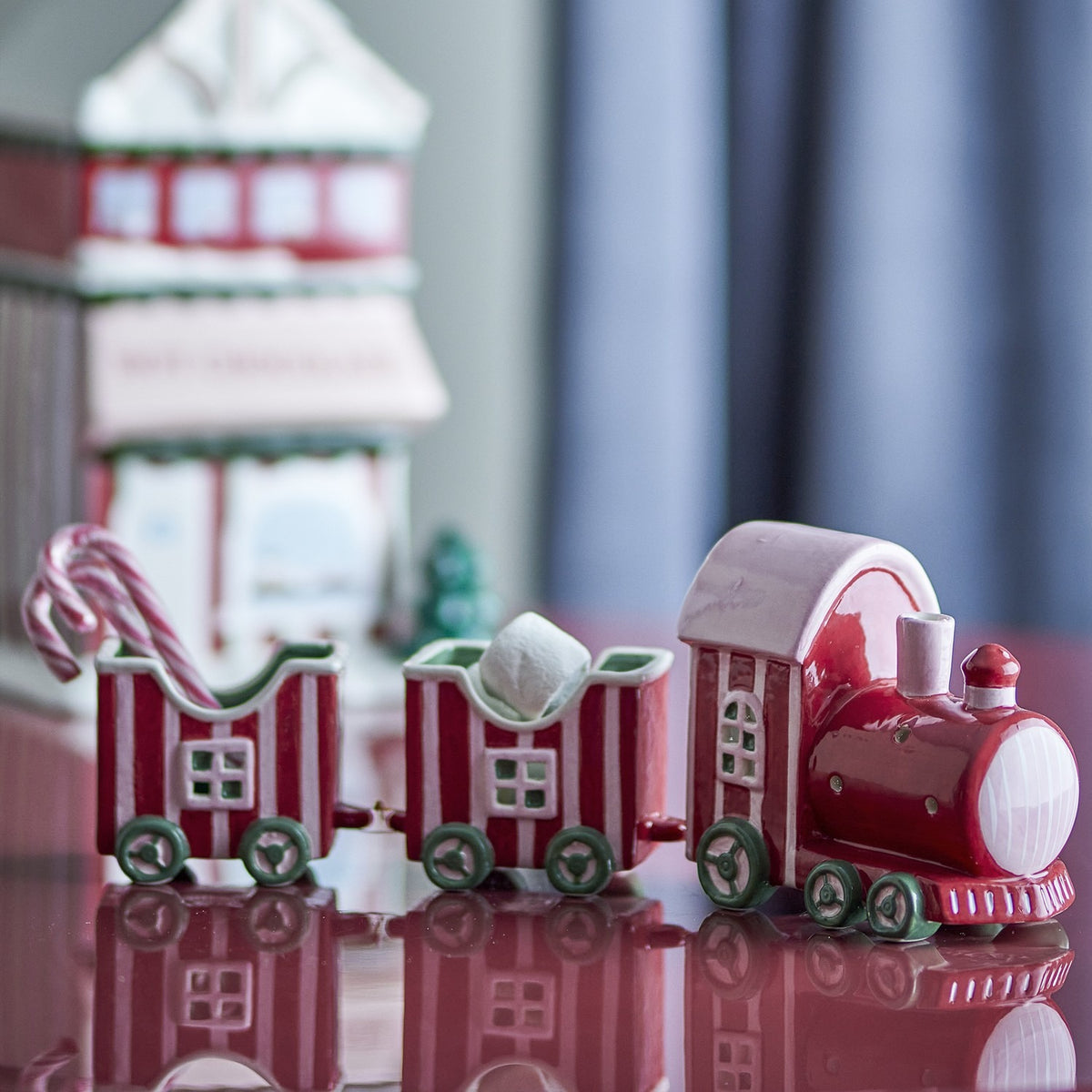 Gloria Striped Ceramic Christmas Decoration in red, a hand-painted dolomite train with a locomotive and two open wagons holding candy canes and a marshmallow, shown on a reflective surface.
