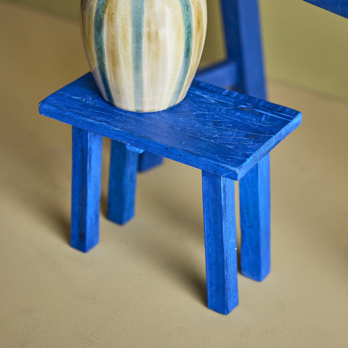 Porir Wooden Pedestal in blue painted reclaimed wood, showing the flat rectangular top on four splayed legs, displaying a striped ceramic vase.