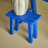 Porir Wooden Pedestal in blue painted reclaimed wood, showing the flat rectangular top on four splayed legs, displaying a striped ceramic vase.