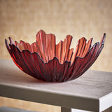 Aila Glass Bowl 31cm in Copper, a wide decorative bowl with a ridged, wavy rim and glowing copper-toned glass, shown on a wooden console against a woven backdrop.
