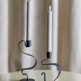 Ponza LED Candles Pack of 2 in beige, tall ribbed paraffin-look columns with flame-shaped tips, shown in black curved metal holders against a neutral curtain backdrop.