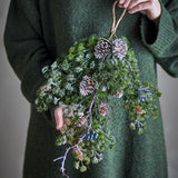 Cedar Christmas Decoration in green, a hanging faux spray with frosted needle tips, pinecones, and berries, held against a green jumper.